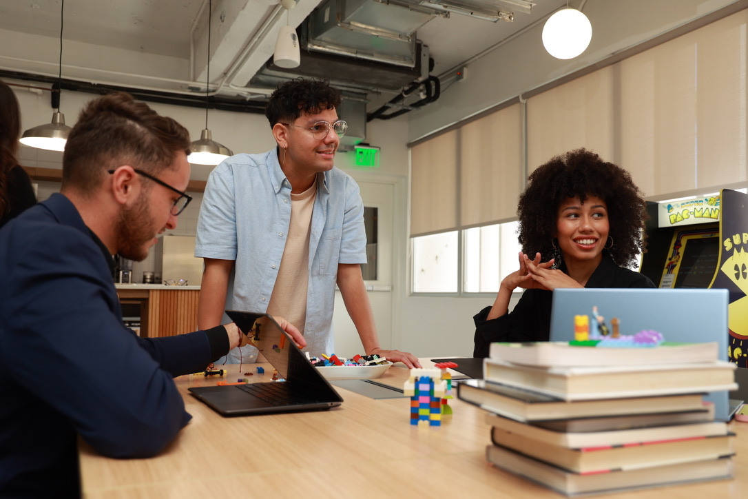 Equipo de Fáctica conversando alrededor de la mesa de trabajo, con libros y LEGO